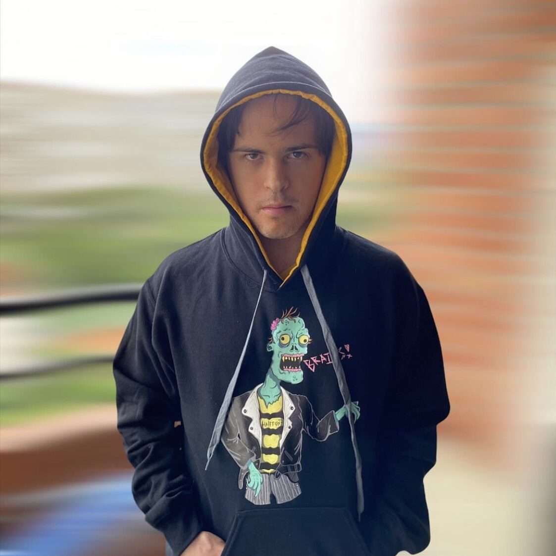 A person with Down Syndrome looking sharply at the camera in Bee-Cool official merch black hoodie with a zombie drawing screaming, "Brains!"