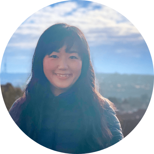 A woman with long black hair smiling outside in a cityscape